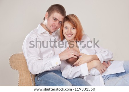 Happy family: mother, father and 10 day old newborn baby sitting on the sofa together. Father holding his wife and baby. Mother holding  and nursing ( breast feeding ) her sleeping baby