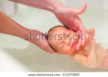 5 days old newborn swimming with help of parents hands for the first time. Baby has neonatal jaundice. Focus on baby head
