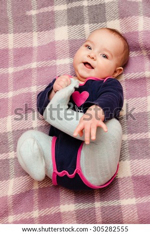 Cute laughing baby in long sleeve body suite and tights lying on his back on warm blanket and playing with legs. Baby looking straight at the camera. Selective focus on baby head.