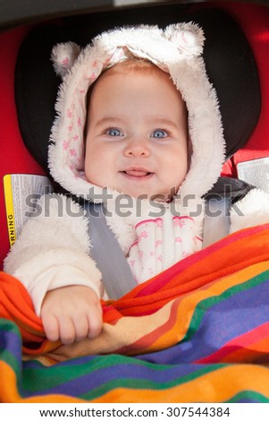 Cute smiling baby girl dressed in fur all-in-one with hood lying in car seat for infants.