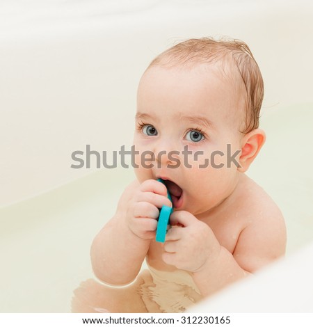 Funny baby sitting in the bathtub, playing and splashing. Bathroom time, washing time. It\'s good to be clean. Baby looking straight at the camera. Selective focus on baby face.