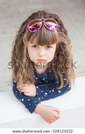 Sad little girl with curly long hair in sunglasses and dress. Sunglasses reflect palm trees. End of vacations.