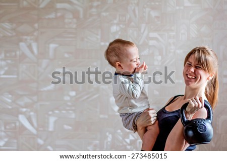 Sportive mother with happy baby and kettlebell in hands. Motherhood is not a cause to let oneself go