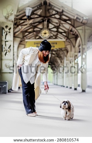 Elegant young woman is bending forward to shih tzu dog under the clock  and inscription 