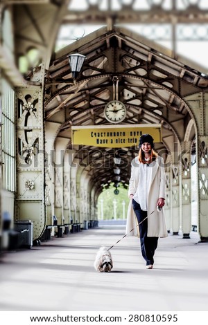Elegant young woman is walking shih tzu dog on the platform under the clock  and inscription 