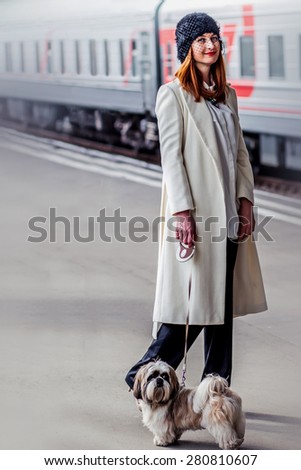 Elegant young woman with hat with veil and shih tzu dog standing near train at the Vitebsk railway station in St.-Petersburg, Russia.