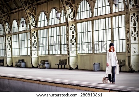 Elegant ginger hair woman in hat with veil is walking shih tzu dog on the platform with beautiful stained-glass windows at the Vitebsk railway station in St.-Petersburg, Russia