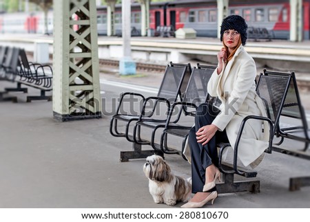 Elegant ginger hair woman with shih tzu dog sitting on the bench while waiting a train at the Vitebsk railway station in St.-Petersburg, Russia.