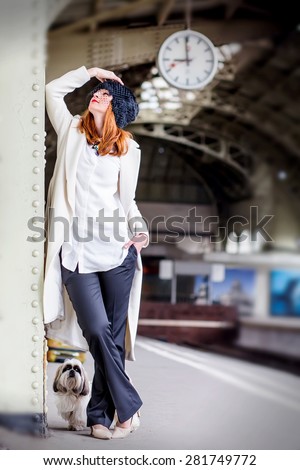 Elegant ginger hair woman with shih tzu dog on the platform under the clock waiting train at the Vitebsk railway station