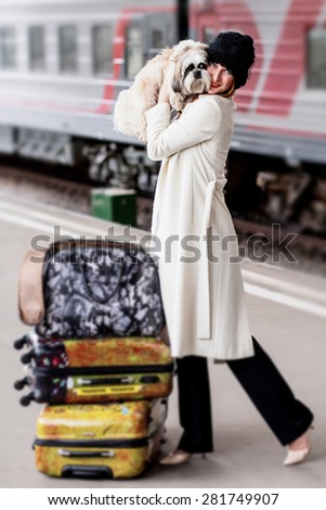 Elegant lady with suitcases and her shih tzu dog in hands on the platform near train at Vitebsk railway station in St.-Petersburg, Russia. Image with selective focus