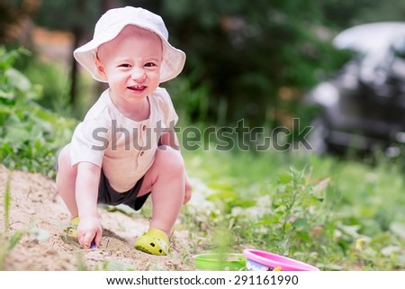 Laughing happy little boy in panama hat playing in sand-box