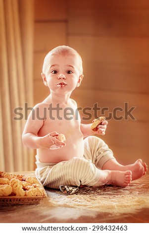 Cute baby on the table with funny face smudgy with flour and homemade cookies in both hands. Image with selective focus and toning