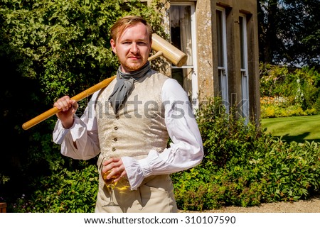 Handsome ginger hair man dressed in regency period costume with glass of sparkling vine and croquet mallet. Image with selective focus