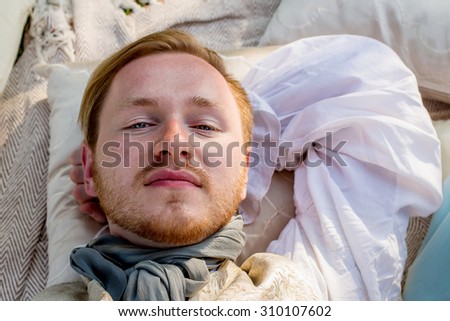 Portrait of lying handsome ginger hair man dressed in regency period costume with sun beam on his face. Image with selective focus