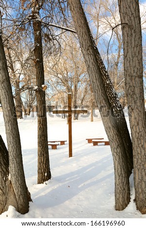 Snow covered cross outdoors among a group of dormant trees on a cold winter day.