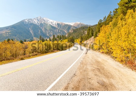 Tree lined mountain road with changing aspens and snow capped mountains.