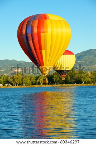 Pair of low flying hot air balloons over water.