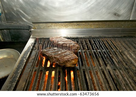 Closeup of a pair of New York Strip steaks cooking over an open flame.