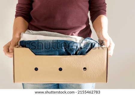 Woman holding cardbox with women's casual all-season clothes.  Storage concept . Reuse, recycle, charity concept. Make donation to poor needy people Foto stock © 