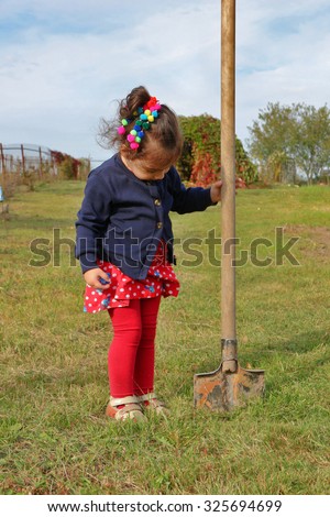 Little girl stands with big garden spade in her hand, stuck in ground. Work in garden