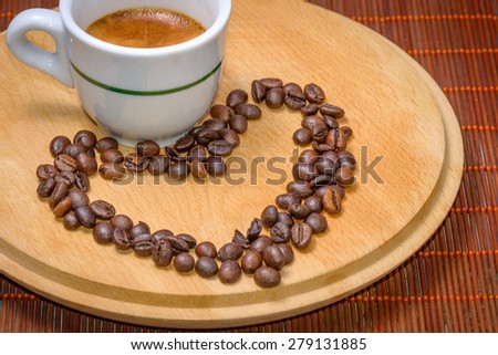 A cup of coffee on wood with seeds around drawing an heart