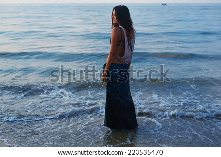 Beautiful slim girl posing on a sea background. Beautiful waves with foam wash her ??feet. Romantic girl looking at the sea.