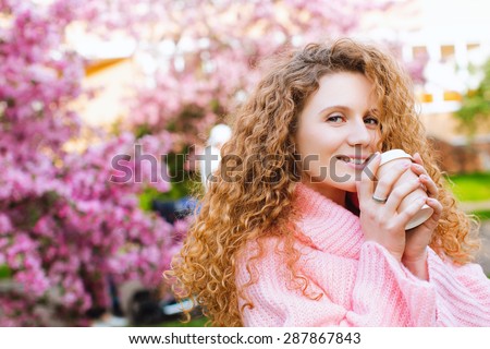 Beautiful curly girl posing on a background of a blossoming rose garden with a coffee in hand. Spring day.