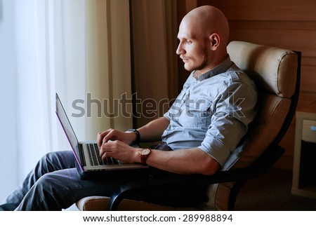 Young successful handsome man working with computer in a hotel room. Businessman traveling with work.