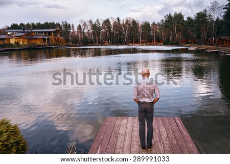The young man, back, stands on the lake and looking at the water.