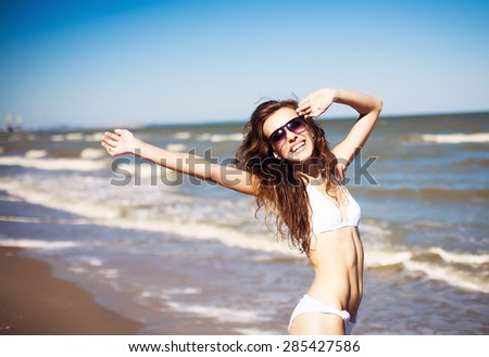 Young, beautiful, slim and sexy woman in bikini on the beach. Travel and Vacation. Freedom Concept. Girl with curly hair and stylish sunglasses having fun in the background of the Caribbean.