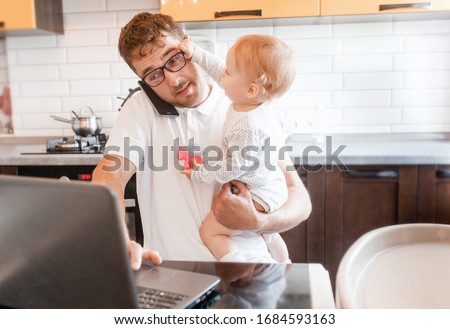 Handsome young man working at home with a laptop with a baby on his hands. Stay home concept. Home office with kids. 