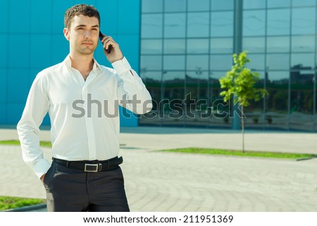 Portrait of young handsome successful business man near blue wall of business center speaking over mobile phone. Outdoor shot
