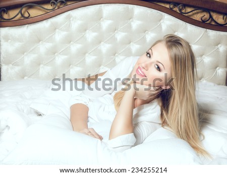 Beautiful young and sexy sensual blond glamorous girl in luxurious bed on white blanket.