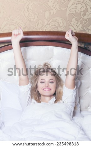 A happy caucasian girl stretching on a bed on a light background. Good morning concept.