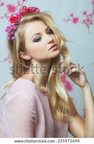 Portrait of romantic tender blond girl with flowers in her hair over pink background.