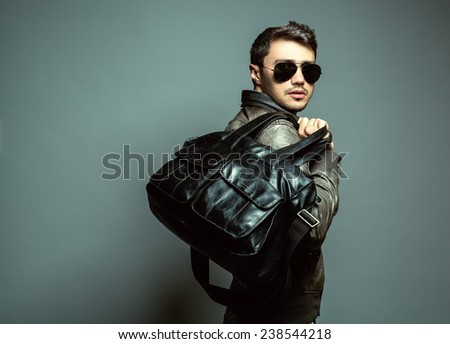 Fashion portrait of handsome man in leather, sunglasses, trendy jacket and black modern bag. Studio shot. Close up.