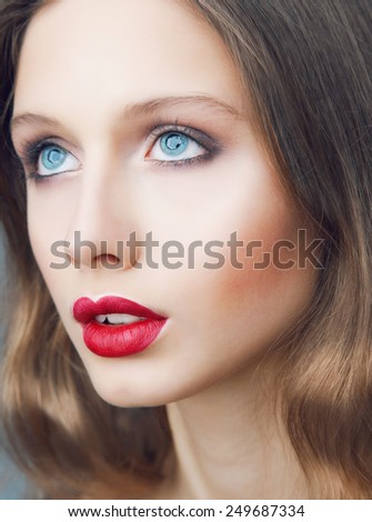 Emotive portrait of young beautiful woman with perfect make up. Red lips and blue eyes.