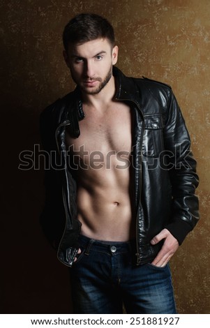 Fashion portrait of handsome athletic young man in trendy casual leather jacket  and jeans over golden background.