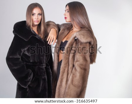 Fashion portrait of two elegant beautiful women in studio on grey background wearing fur coats .