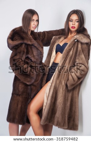 Fashion portrait of two elegant woman in fur mink coat over white background.