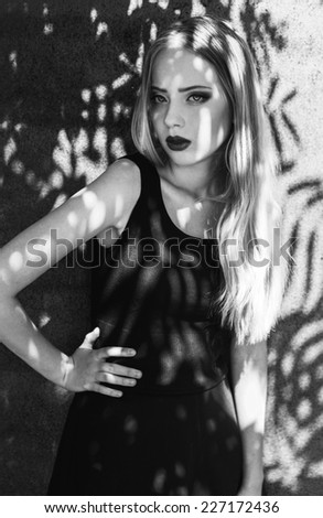 Fashion portrait of beautiful blond-haired girl in trendy black crop top and skirt posing over rusty metal background.