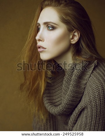 Studio shot. Emotive portrait of fashionable model with long curly red hair and natural make-up posing over wooden background. Perfect skin and green eyes. Urban style.