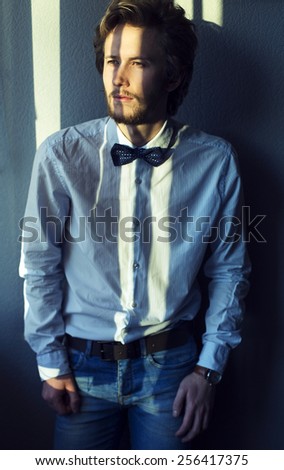 Emotive portrait of handsome young man in white shirt and black bow-tie posing over gray background.  Urban style. Studio shot