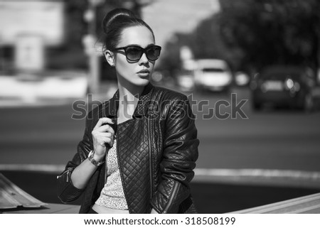 Female beauty concept. Portrait of fashionable young girl in casual black jeans, black jacket, white crop-top, sunglasses and small  bag posing on the street.  Vogue style. outdoor shot