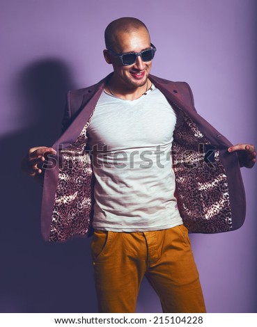 Young handsome man in trendy glasses, purple jacket, white undervest and orange briefs posing on purple background. Studio shot. Copy space.