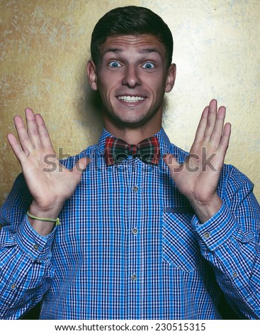 WOW concept. Emotive portrait of a funny hipster handsome young man in plaid blue shirt and Scottish tie-bow posing over golden background. Studio shot. Close-up