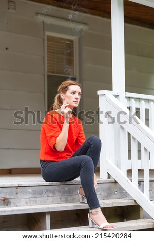 Beautiful young woman sitting outside smoking cigarette