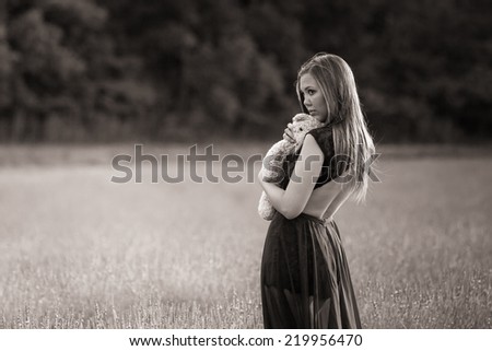 Beautiful young woman wearing black dress holding teddy bear in lavender field