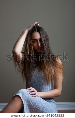 Portrait of gorgeous young woman with long brown ombre hair and blue eyes. Sitting on hardwood floor, wearing sleeveless grey fitted dress.