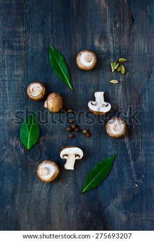 Top view of fresh mushrooms with spices and herbs on dark wooden background.